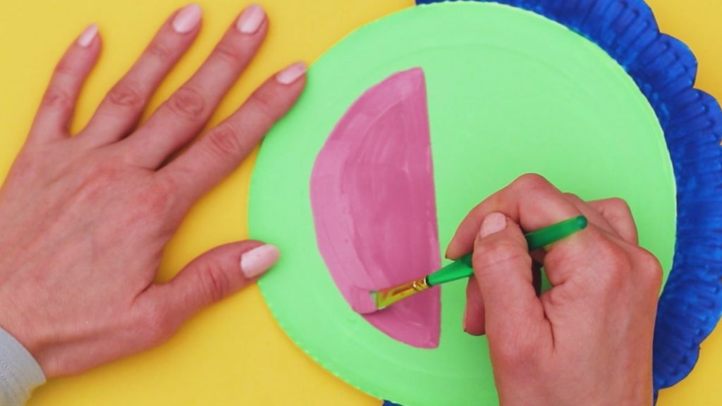 Image showing a pink semi circle being painted onto the main paper plate.