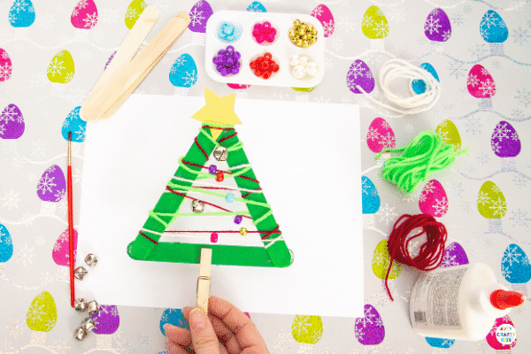 Yarn Wrapped Musical Popsicle Stick Christmas Tree Craft for Kids - Create this easy Christmas Ornament with your kids this Christmas. The Christmas Tree craft doubles up as a jingly musical instrument that will be fun going all day long.