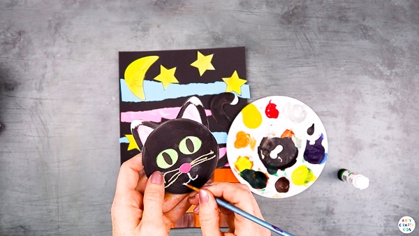 Add detail to the black cats face with whiskers, eyes and a cute little nose.