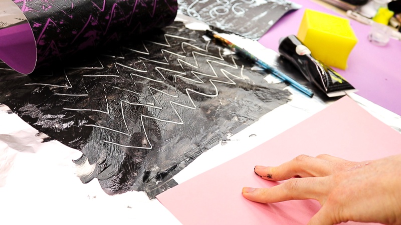 Image showing a piece of purple card stock being peeled gently away from a zig-zag print on the aluminium foil. A mono print can be revealed.