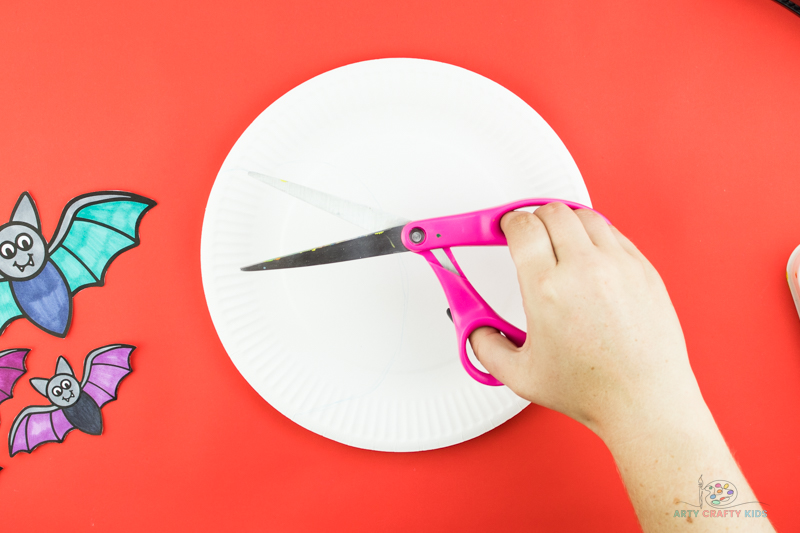 Image showing a hand with a pair of scissors cutting out the paper plate into a moon crescent.