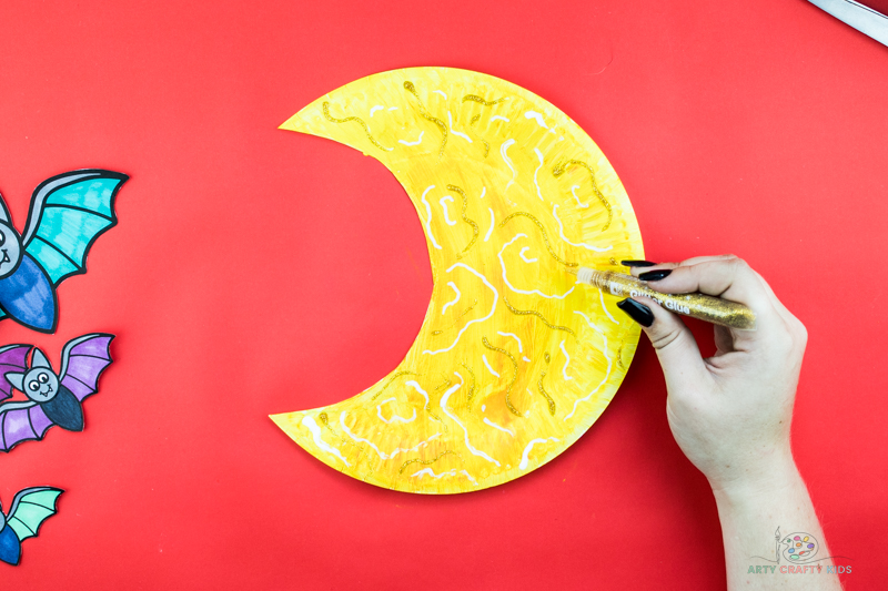 Image showing a hand decorating a yellow moon with golden glitter glue.