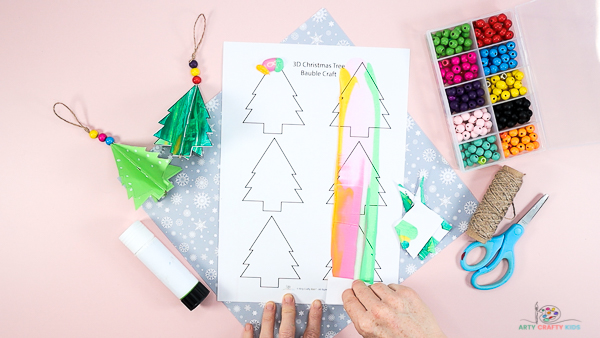 Image showing a hand scraping paint with scrap cardboard in a downwards motion across the Christmas tree template.