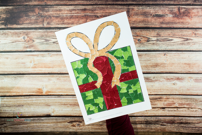Image showing gold glittery torn paper filling the boy elements of the present, with a red paper cross and green present.
