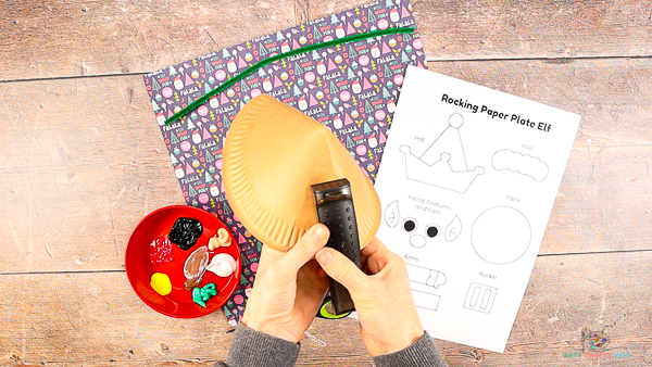 Image showing hands with a stapler securing the folded paper plate in place.