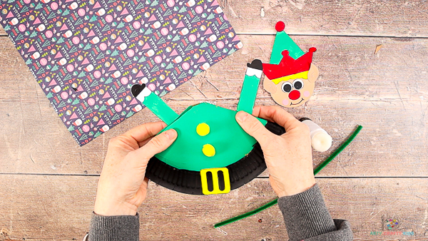 Image showing hands securing a pair of elf's arms to the back of the paper plate.