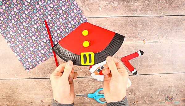 Image showing hands holding a painted paper plate with an added buckle and two pom-pom buttons.