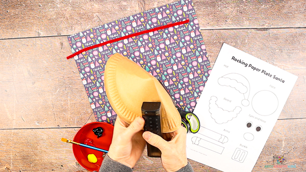 Image showing hands stapling the folded paper plate in place.