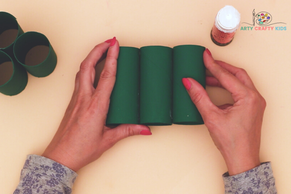 Image showing hands pushing together three green paper rolls to form the base of the Christmas tree.