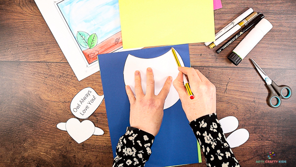 Image showing hands tracing around the body of the owl onto blue card stock.