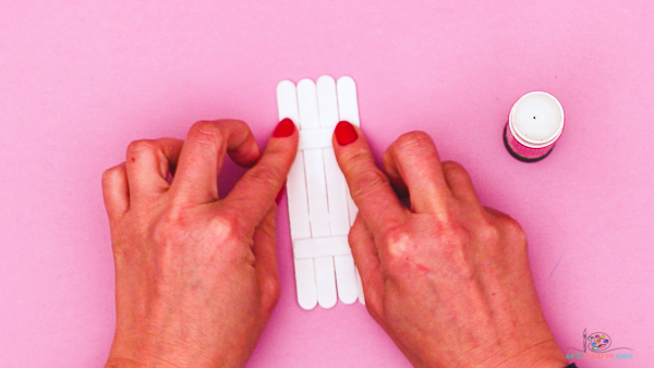 Image showing hands securing two short popsicle sticks across the group of four.