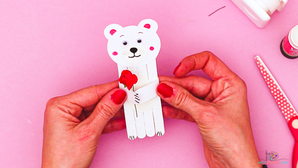 Image showing hands securing arms to the back of the popsicle stick polar bear to complete the craft.