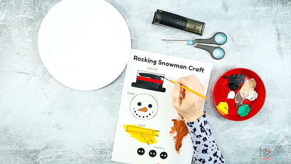 Image showing a hand painting the top hat and elements within the snowman printable template.