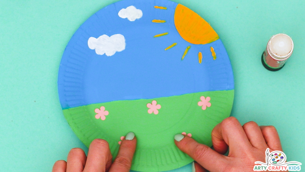 Image showing hands sticking pink flowers on the grassy area of the paper plate.