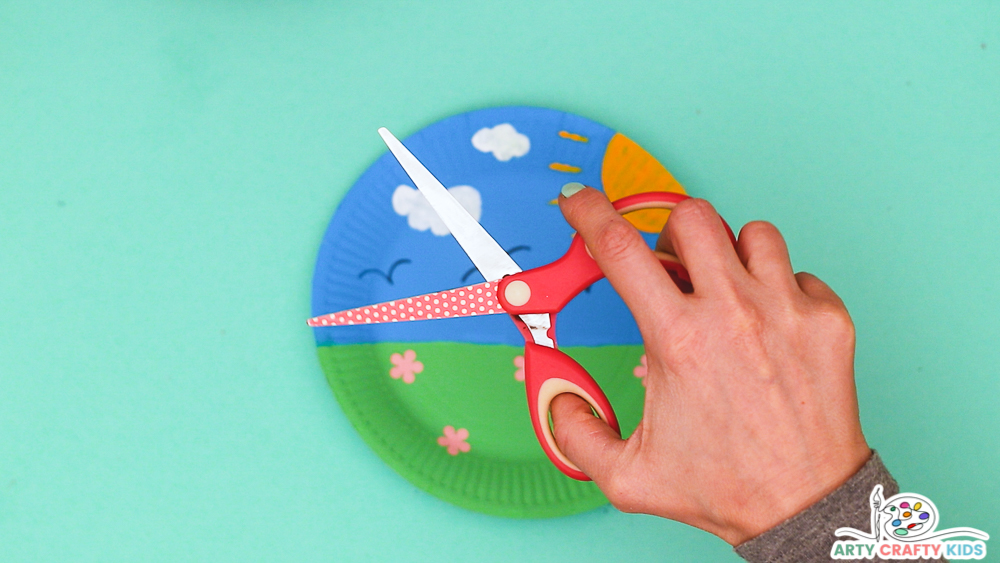Image showing hands holding an open pair of scissors above the paper plate to suggest creating an opening within the paper plate.