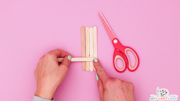 Image showing hands preparing the popsicle sticks into a group of four with a single stick placed across.