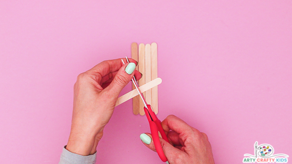 Image showing hands cutting a popsicle stick down to size to match the width of the Popsicle sticks.