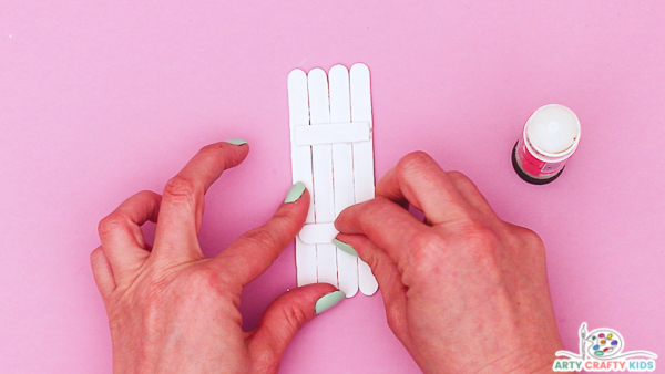 Image showing hands  gluing supporting sticks across the group of four Popsicle sticks.