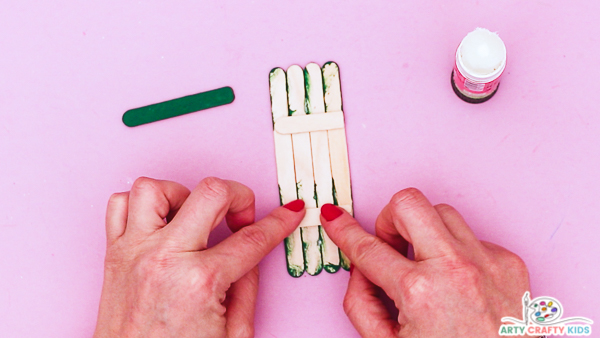 Image showing hands securing the group of four Popsicle sticks with two shorter pieces glued across the back.