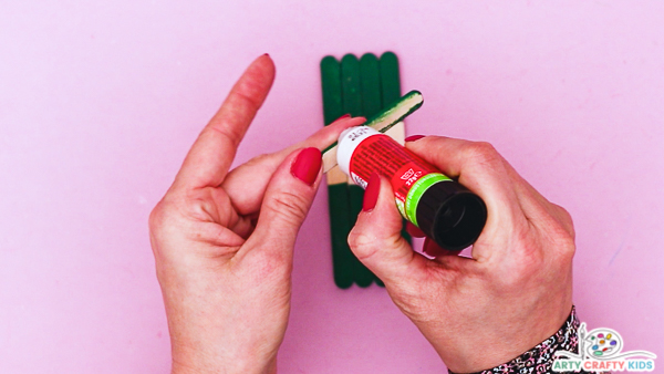 Image showing hands applying glue to the extended short piece to complete the hat.