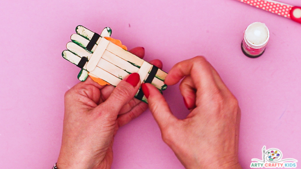 Image showing hands wrapping a piece of black ribbon to the back of the popsicle stick.