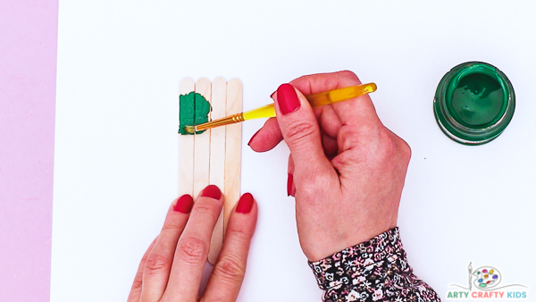 Image showing hands painting the group of four Popsicle sticks an emerald green.