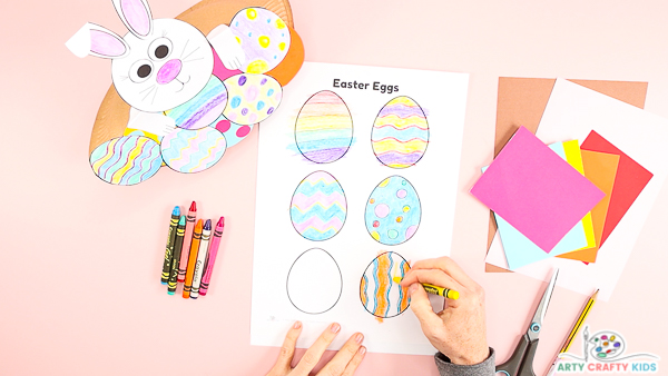 Image showing hands designing and coloring in a series of blank Easter eggs from a printable template.