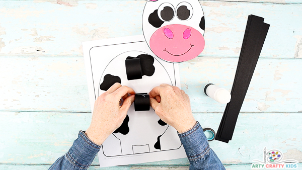 Image showing hands sticking two paper loops onto the body of the cow.