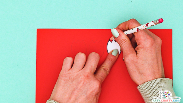 Image showing a hand tracing around a tulip from the printable template onto red card stock.