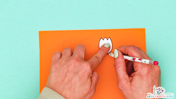 Image showing a hand tracing around a tulip from the printable template onto orange card stock.