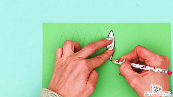 Image showing a hand tracing around a leaf from the printable template onto green card stock.