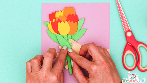 Image showing hands glueing the final leaf to a bouquet of nine tulips glued to the inside of the handprint.