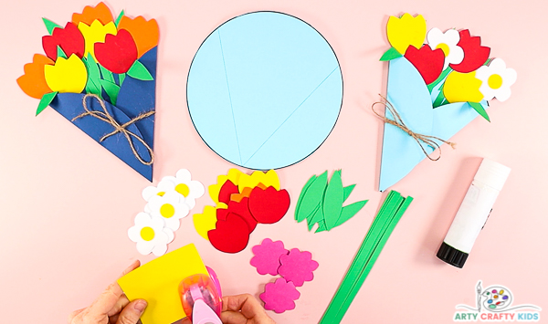 Image showing multiple cut out colorful flowers, green leaves and green paper strips. 

A hand is using a hole punch to create yellow circular center's for the flower's.