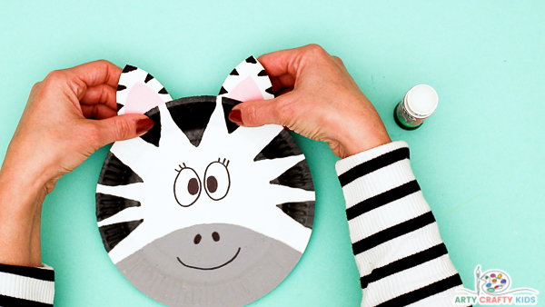 Image showing hands securing the ears to the back of the paper plate zebra craft.
