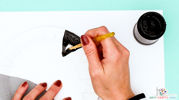 Image showing hands painting a black triangular shape onto the paper plate - this will become the zebra's stripes.