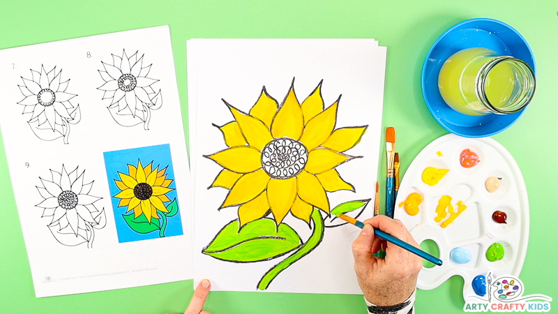 Image showing a hand painting the leaves of the sunflower bright green. The petals have been painted yellow.
