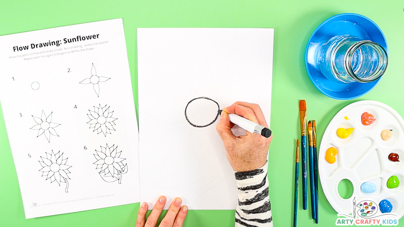 Image showing a hand following step one of the how to draw a sunflower. 

A hand is drawing a circle in the center of the sheet.