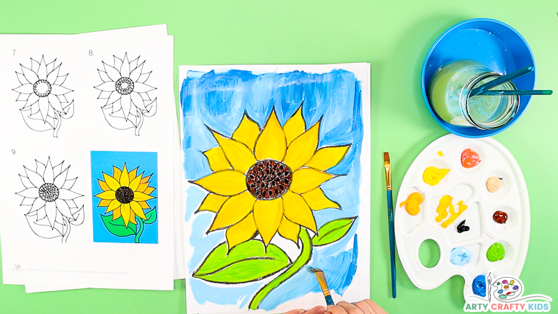 Image showing a hand painting the white space surrounding the sunflower sky blue.