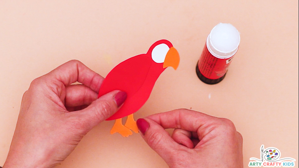 Image showing a hand assembling the parrot, adding a beak, eye and legs to the red body.