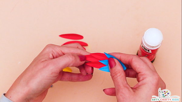 Image showing hands creating a large tail feather out of layered red and blue feathers.