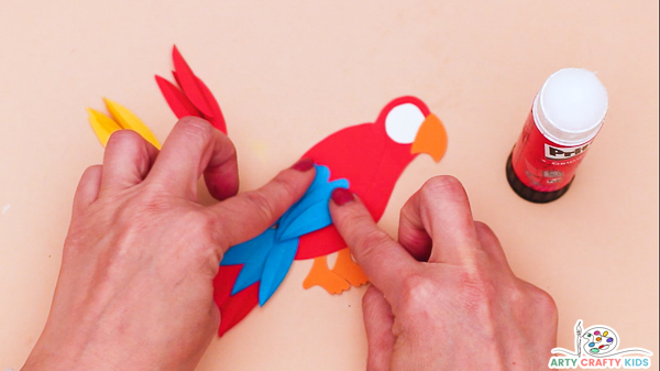 Image showing a hand glueing blue wing feathers onto the body of the parrot.