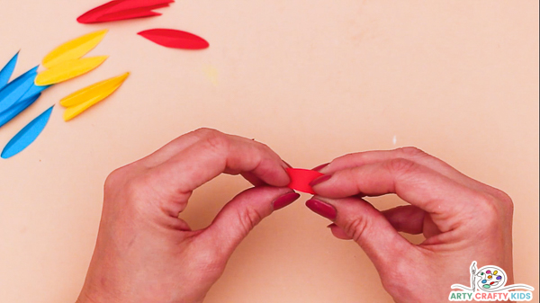 Image showing hands folding a collection of cut out paper feathers in half. The image shows red, yellow and blue feathers.