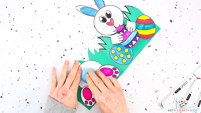 This image features step 13 and shows hands glueing a large blue pom-pom to the bunny's bottom!