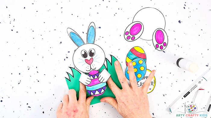 This image features step 11 and shows a pair of hands affixing the arms and eggs to the front of the Easter card - creating a pop-up effect.