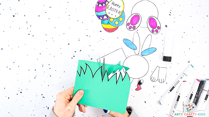 This image features Step 4 with a hand cutting along the grassy edge of the Easter card printable template.