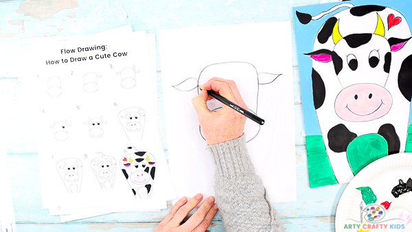 Image showing step 2: A hand drawing a pair of pointy ears on either side of the cows head.
