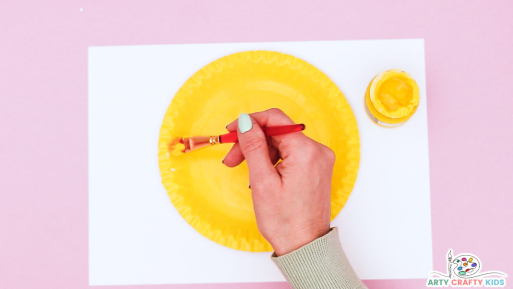 Image showing a hand painting a paper plate yellow.