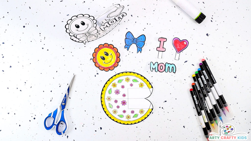 Image featuring the elements of the printable Mother's Day cut out on a table with pens, scissors and a glue stick surrounding it.