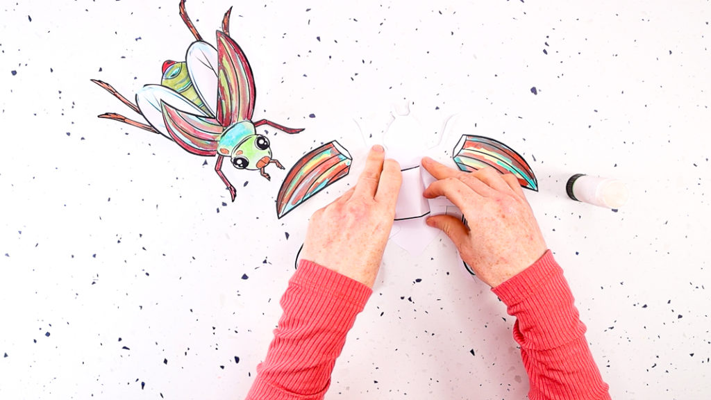 Image featuring a hand glueing the finger-puppet element to the back of the beetles body.