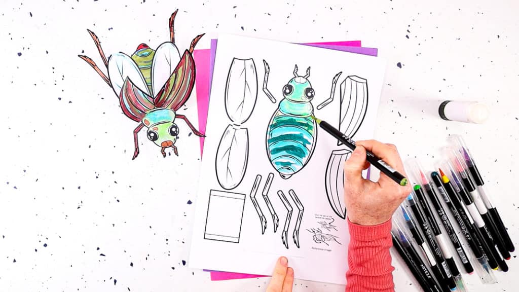 Image featuring a hand coloring the beetle template in various shades of green. 